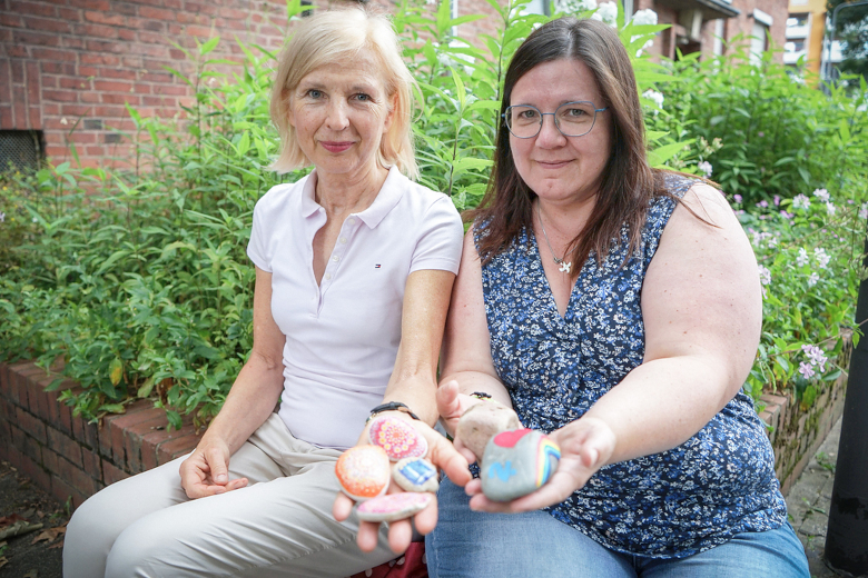 Verena Maria Kitz (l.), Leiterin des Zentrums für Trauerseelsorge des Bistums Limburg, und Judith Poser, Trauerbegleiterin im Zentrum, halten bunt bemalte Trauersteine in Andenken an Verstorbene. 